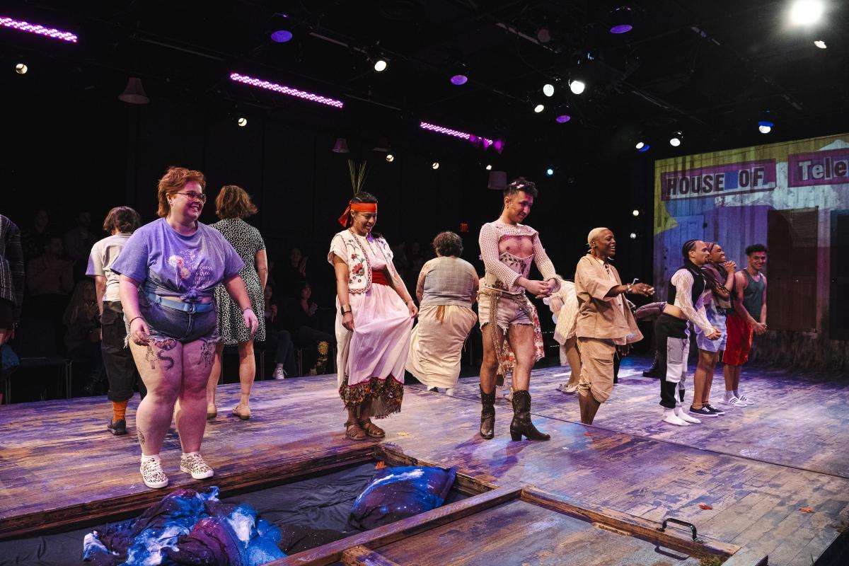 Performers stand on stage in a line jumping. In the background, the backdrop reads House of Telescopes.